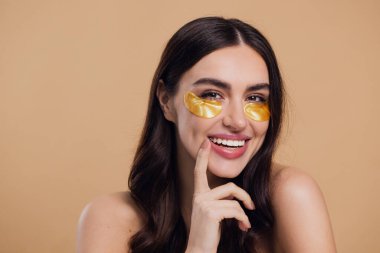 Saf, güzel, kibar bir kadının güzel görüntüsü. Çıplak, soyutlanmış bir kamera gibi duruyor. Bej arka planda altın rengi bantlarla cildine dikkat et.