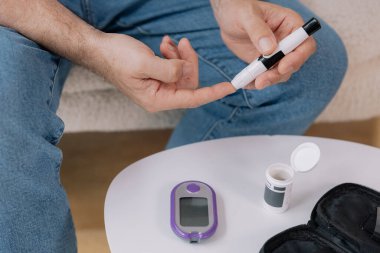 Tekerlekli sandalyedeki diyabetik kıdemli adam kan şekeri seviyesini parmak ölçer, glikoz ölçer. Tip 1 diyabeti olan yaşlı bir adam evde kan şekeri monitörü kullanıyor..