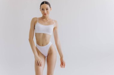 Manzarayı kapat. Zayıf vücutlu güzel bir kadın ve beyaz stüdyo arka planında iç çamaşırlarıyla poz veren mükemmel bir karın..