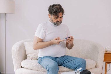 Tekerlekli sandalyedeki diyabetik kıdemli adam kan şekeri seviyesini parmak ölçer, glikoz ölçer. Tip 1 diyabeti olan yaşlı bir adam evde kan şekeri monitörü kullanıyor..