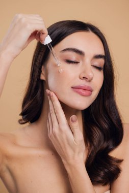 Bej arka planda Serum Bırakan Kadın. Pipette 'ten Serum Kolajeni Nemlendirici kullanan Avrupalı Kız. Yakın plan. Pozitif Gülen Güzel Kadın Portresi. Yüz Cildi Bakımı Konsepti