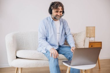Dedem dizüstü bilgisayar ve kulaklık kullanıyormuş. Koltukta oturuyormuş. Evden çalışan kıdemli adam, çevrimiçi toplantı, görüntülü konuşma, kopyalama alanı
