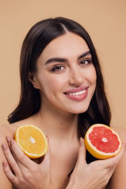 Genç bir kadının portresi, portakal rengi greyfurt gülümseyen dişlerin yarısını beslenen vejetaryen vitamin yaz vitamini, saç bakımı, doğal organik vegan narenciye bej arka planda.