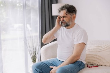 Ev, son sınıf öğrencisi ve stres, duygusal çatışma ve geçici baş dönmesi için kanepede baş ağrısı. Oturma odası, kanepe ve evde emeklilikten doğan acı, migren ve endişe içinde yaşlı bir adam.