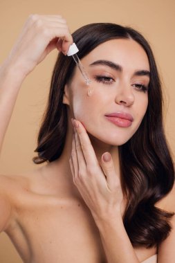 Bej arka planda Serum Bırakan Kadın. Pipette 'ten Serum Kolajeni Nemlendirici kullanan Avrupalı Kız. Yakın plan. Pozitif Gülen Güzel Kadın Portresi. Yüz Cildi Bakımı Konsepti