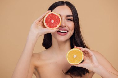 Genç bir kadının portresi, portakal rengi greyfurt gülümseyen dişlerin yarısını beslenen vejetaryen vitamin yaz vitamini, saç bakımı, doğal organik vegan narenciye bej arka planda.