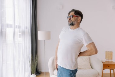 Hasta, mutsuz, yaşlı bir adam, kas hasarına dokunuyor. Sırtında ağrılar var. Evde sırt ağrısı. Fiziksel yaralanma ve sağlık sorunları