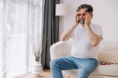 Ev, son sınıf öğrencisi ve stres, duygusal çatışma ve geçici baş dönmesi için kanepede baş ağrısı. Oturma odası, kanepe ve evde emeklilikten doğan acı, migren ve endişe içinde yaşlı bir adam.