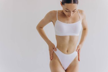 Manzarayı kapat. Zayıf vücutlu güzel bir kadın ve beyaz stüdyo arka planında iç çamaşırlarıyla poz veren mükemmel bir karın..