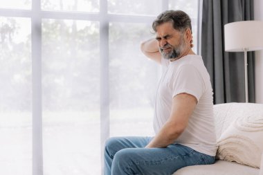 Üst sınıflardan biri içeride oturuyor, boynu ağrıyormuş gibi görünüyor. Üzüntülü bir ifadeyle boynunu tutuyor, rahatsız olduğunu gösteriyor..