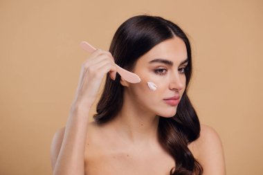 Yarı çıplak kadın, güzellik için yüz ve fırça kremi, kuaför ve cilt bakımı bej arka planda. Mutlu model, yüz losyonu ve dermatoloji, kolajen ve mutluluğun gülümsemesi için makyaj malzemesi.