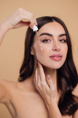 Bej arka planda Serum Bırakan Kadın. Pipette 'ten Serum Kolajeni Nemlendirici kullanan Avrupalı Kız. Yakın plan. Pozitif Gülen Güzel Kadın Portresi. Yüz Cildi Bakımı Konsepti