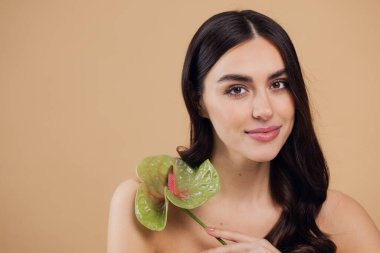 Bej renkli stüdyo arka planında izole edilmiş çiçekle poz veren çekici genç bir kadının güzel portresi.