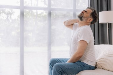 Üst sınıflardan biri içeride oturuyor, boynu ağrıyormuş gibi görünüyor. Üzüntülü bir ifadeyle boynunu tutuyor, rahatsız olduğunu gösteriyor..
