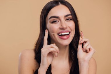 Oral Bakım. Güzel kadın diş ipi kullanıyor ve kameraya gülümsüyor, Mutlu Çekici Kadın Diş Temizleme, Bej Stüdyo Arkaplanına sarılı, Kopyalama Alanı