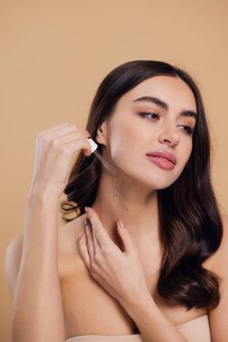 Bej arka planda Serum Bırakan Kadın. Pipette 'ten Serum Kolajeni Nemlendirici kullanan Avrupalı Kız. Yakın plan. Pozitif Gülen Güzel Kadın Portresi. Yüz Cildi Bakımı Konsepti