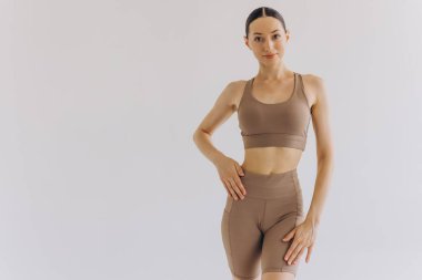 Beyaz arka planda bej renkli spor giysili zayıf bir kadın izole edilmiş. Düz göbekli, kaslı, zayıf, çekici bir kadın. Uzayı metin için kopyala. Vücut bakımı, sağlıklı ve sportif yaşam, saç aldırma, yoga konsepti