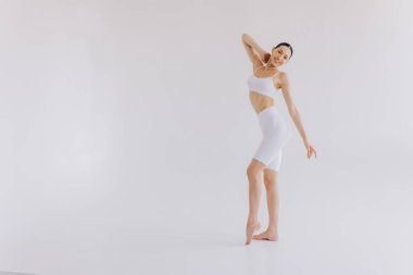 Beyaz arka planda beyaz spor giysili zayıf bir kadın var. Düz göbekli, kaslı, zayıf, çekici bir kadın. Uzayı metin için kopyala. Vücut bakımı, sağlıklı ve sportif yaşam, saç aldırma, yoga konsepti