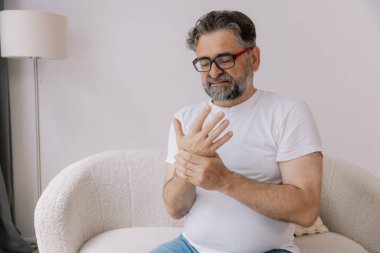 Artrit belirtileri. Gözlüklü yaşlı adam evde acı çekiyor.