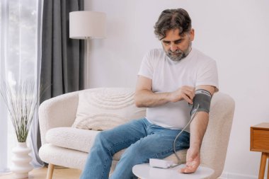 Evdeki kanepede oturmuş, tansiyonunu ölçen, gri saçlı, son sınıf öğrencisi. Modern tonometre kullanan emekli, hipertansiyon deneyimi yaşayan, kopyalama alanı