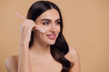 Yarı çıplak kadın, güzellik için yüz ve fırça kremi, kuaför ve cilt bakımı bej arka planda. Mutlu model, yüz losyonu ve dermatoloji, kolajen ve mutluluğun gülümsemesi için makyaj malzemesi.