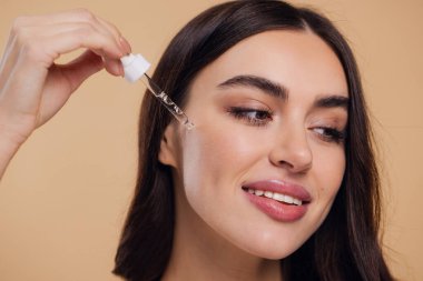 Bej arka planda Serum Bırakan Kadın. Pipette 'ten Serum Kolajeni Nemlendirici kullanan Avrupalı Kız. Yakın plan. Pozitif Gülen Güzel Kadın Portresi. Yüz Cildi Bakımı Konsepti