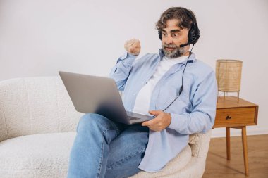 Dedem dizüstü bilgisayar ve kulaklık kullanıyormuş. Koltukta oturuyormuş. Evden çalışan kıdemli adam, çevrimiçi toplantı, görüntülü konuşma, kopyalama alanı