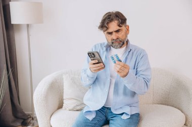 Yaşlı bir adam kanepede tek başına oturuyor. Bir hasta gözlük takıyor. Akıllı telefondan talimatları okuyor.