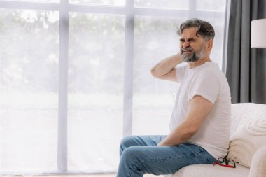 Üst sınıflardan biri içeride oturuyor, boynu ağrıyormuş gibi görünüyor. Üzüntülü bir ifadeyle boynunu tutuyor, rahatsız olduğunu gösteriyor..
