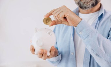 Kıdemli adam kumbarayı elinde tutuyor. Bozuk paralı yaşlı erkek, bitcoin, finans, tasarruf, gelir kavramı, kopyalama alanı