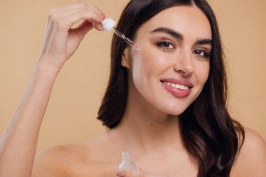 Bej arka planda Serum Bırakan Kadın. Pipette 'ten Serum Kolajeni Nemlendirici kullanan Avrupalı Kız. Yakın plan. Pozitif Gülen Güzel Kadın Portresi. Yüz Cildi Bakımı Konsepti