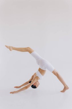 Uzun boylu, zayıf vücutlu, jimnastik ya da jimnastik ve esneme sporu yapan genç bir kadın. Beyaz spor elbise giyen bir kız. Sporcu kadın ellerinin üstünde ya da baş aşağı duruyor.