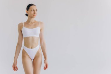 İnce vücutlu güzel bir kadının portresi. Beyaz stüdyo arka planında fotokopi alanı ile poz veriyor.