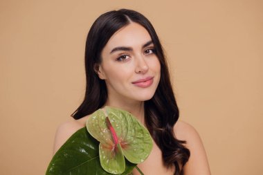 Yüzü ve vücudu yeşil olan genç ve güzel bir kadın. Cilt bakımı güzellik tedavisi konsepti. Yeşil izinli kapanış kızı. Stüdyoda bej arka planda poz veren beyaz bir model.