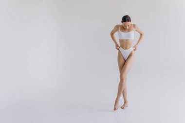 İnce vücutlu, beyaz stüdyo arka planında fotokopi aletiyle poz veren güzel bir kadının tam boy portresi.