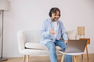 Dedem dizüstü bilgisayar ve kulaklık kullanıyormuş. Koltukta oturuyormuş. Evden çalışan kıdemli adam, çevrimiçi toplantı, görüntülü konuşma, kopyalama alanı