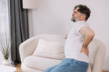 Evdeki kanepede sırt ağrısı çeken yaşlı bir adamın arka görüntüsü, reklamınız için yer açın.