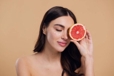 Göz Cildi Bakıcı Kadın. Greyfurt Tutan Güzel Genç Kadın Göz Altındaki Cilde Göz Kremi Döküyor. Antiyaj Tedavisi Konsepti. Yüksek Kalite