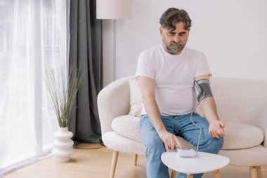 Evdeki kanepede oturmuş, tansiyonunu ölçen, gri saçlı, son sınıf öğrencisi. Modern tonometre kullanan emekli, hipertansiyon deneyimi yaşayan, kopyalama alanı