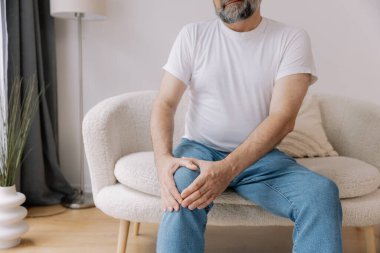 Ev, diz ağrısı ve koltukta eklem iltihabı, kemik erimesi ve fibromiyalji olan yaşlı bir adam. Rahatlama, kas gerilimi ve kaza ya da emeklilikte yaralanma için eklem masajı yapan yaşlı erkek.