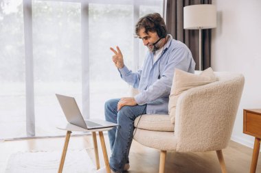 Dedem dizüstü bilgisayar ve kulaklık kullanıyormuş. Koltukta oturuyormuş. Evden çalışan kıdemli adam, çevrimiçi toplantı, görüntülü konuşma, kopyalama alanı