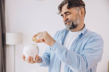 Kıdemli adam kumbarayı elinde tutuyor. Bozuk paralı yaşlı erkek, bitcoin, finans, tasarruf, gelir kavramı, kopyalama alanı