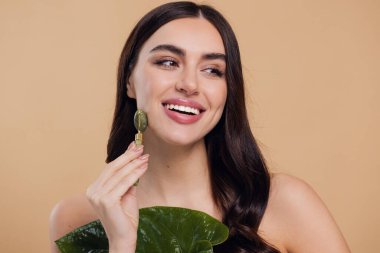 Mükemmel ciltli güzel bir kadının yarı çıplak portresini kapat. Bej arka planda doğal kuvars taşıyla yüz masajı yap..