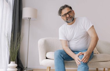 Ev, diz ağrısı ve koltukta eklem iltihabı, kemik erimesi ve fibromiyalji olan yaşlı bir adam. Rahatlama, kas gerilimi ve kaza ya da emeklilikte yaralanma için eklem masajı yapan yaşlı erkek.