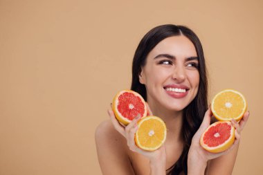 Genç bir kadının portresi, portakal rengi greyfurt gülümseyen dişlerin yarısını beslenen vejetaryen vitamin yaz vitamini, saç bakımı, doğal organik vegan narenciye bej arka planda.