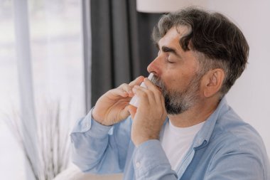 Evde burun spreyi kullanarak grip ve soğuk algınlığı geçiren yaşlı, olgun, hasta bir adam. rhinitis, ilaç ve sağlık hizmeti kavramı