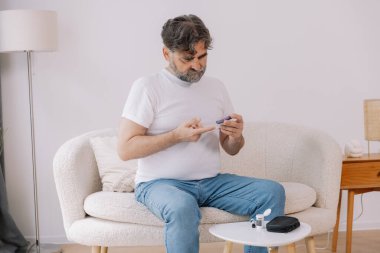 Tekerlekli sandalyedeki diyabetik kıdemli adam kan şekeri seviyesini parmak ölçer, glikoz ölçer. Tip 1 diyabeti olan yaşlı bir adam evde kan şekeri monitörü kullanıyor..