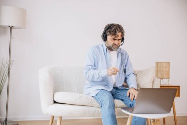 Dedem dizüstü bilgisayar ve kulaklık kullanıyormuş. Koltukta oturuyormuş. Evden çalışan kıdemli adam, çevrimiçi toplantı, görüntülü konuşma, kopyalama alanı