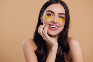 Saf, güzel, kibar bir kadının güzel görüntüsü. Çıplak, soyutlanmış bir kamera gibi duruyor. Bej arka planda altın rengi bantlarla cildine dikkat et.