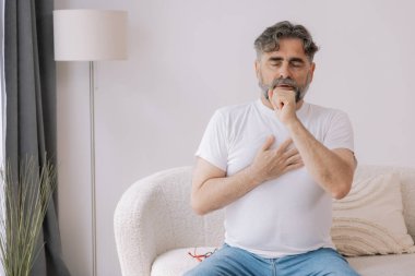 Hasta, öksürük ve kanepede yatan alerji, grip ya da soğuk algınlığı olan yaşlı bir adam. Hastalık, göğüs ağrısı ve astım, enfeksiyon ve COVID 19 virüsü olan yaşlı bir kişi.